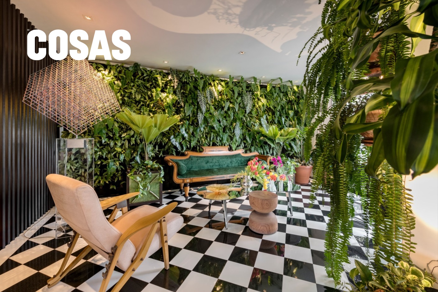 La mesa circular con tapa de espejo, el sillón Biedermeier en terciopelo verde, un banco de tronco natural y la escultura giratoria de Alois Kronschlaeger conforman un escenario donde luz, arte y vegetación dialogan.