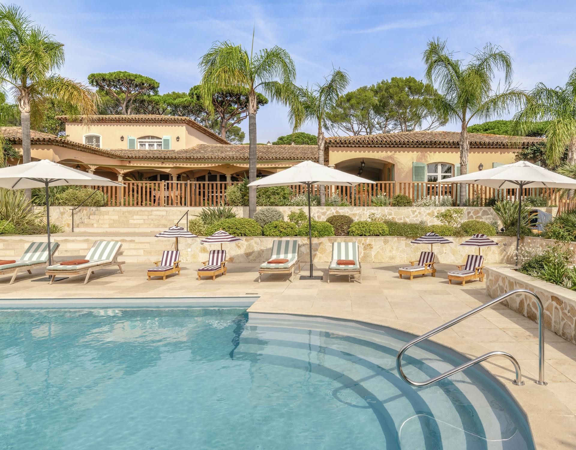 Piscina exterior rodeada de palmeras y arquitectura provenzal, un oasis de calma donde el tiempo se desacelera bajo el sol de la Riviera.
