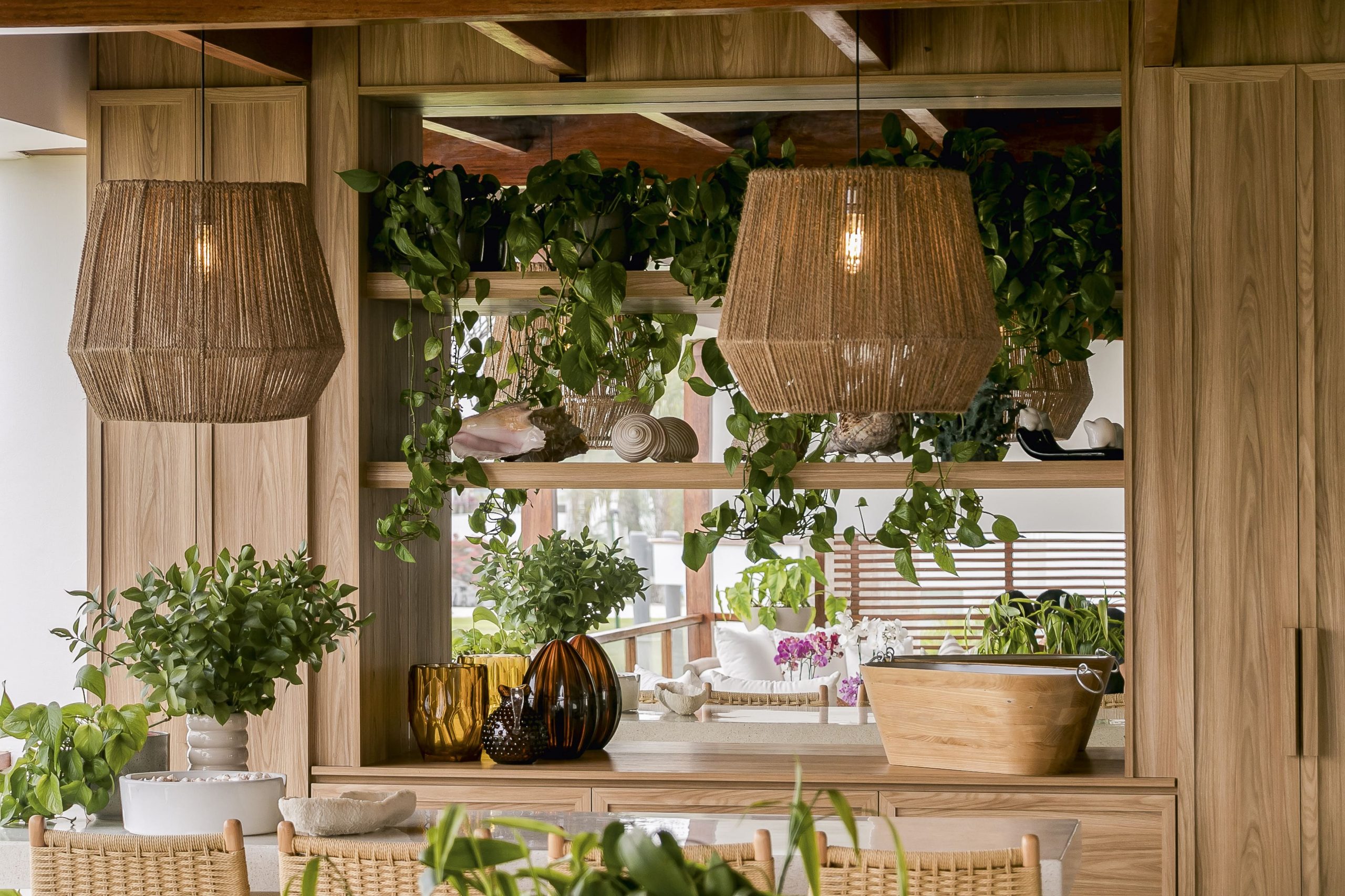 La madera y las fibras naturales construyen un ambiente cálido y ordenado. La vegetación integrada y las lámparas colgantes aportan textura y una luz suave que acompaña el uso cotidiano.