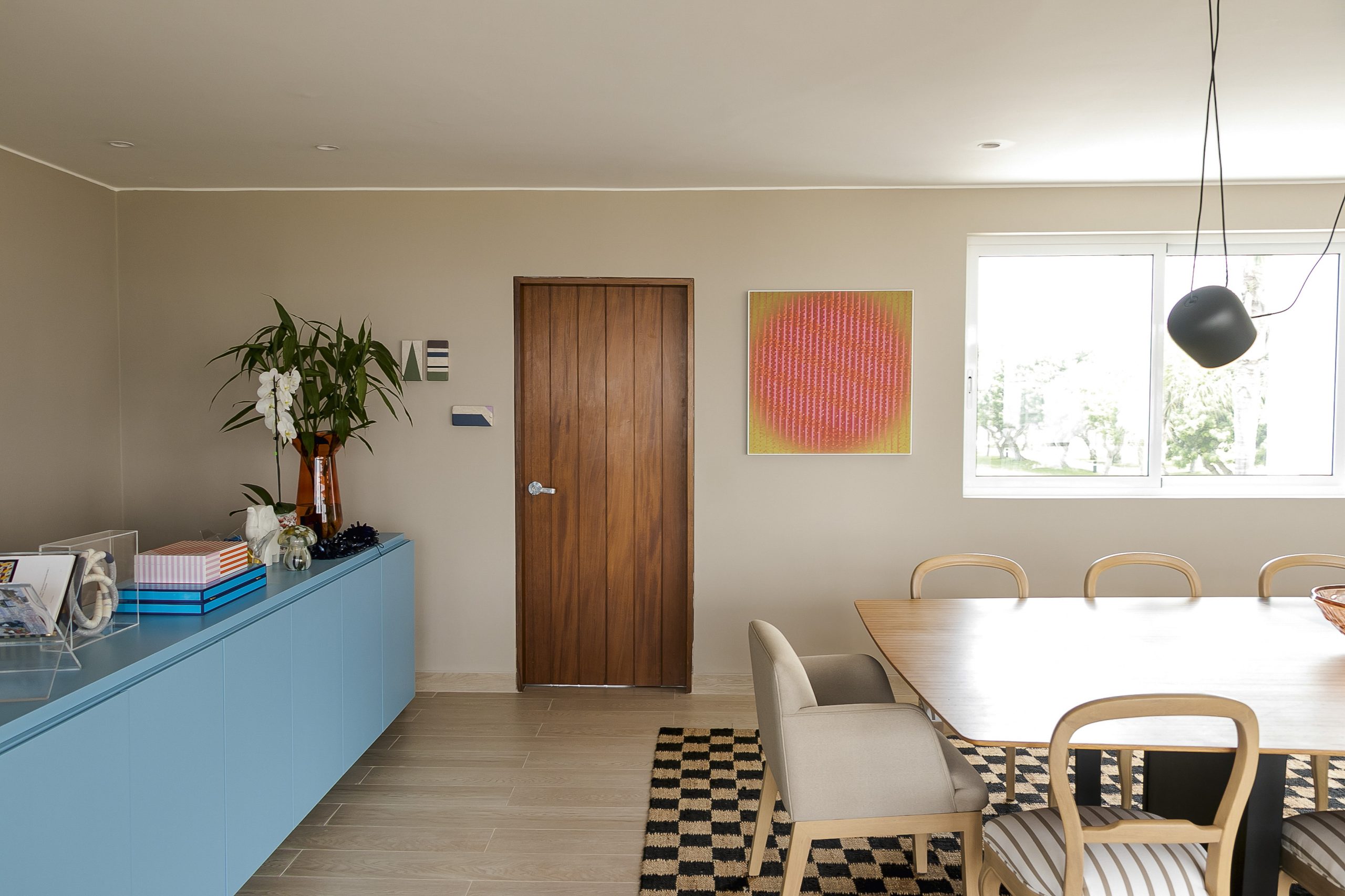 El comedor se organiza a partir de una paleta serena donde la madera, los textiles claros y el acento gráfico de la alfombra marcan el ritmo del espacio.