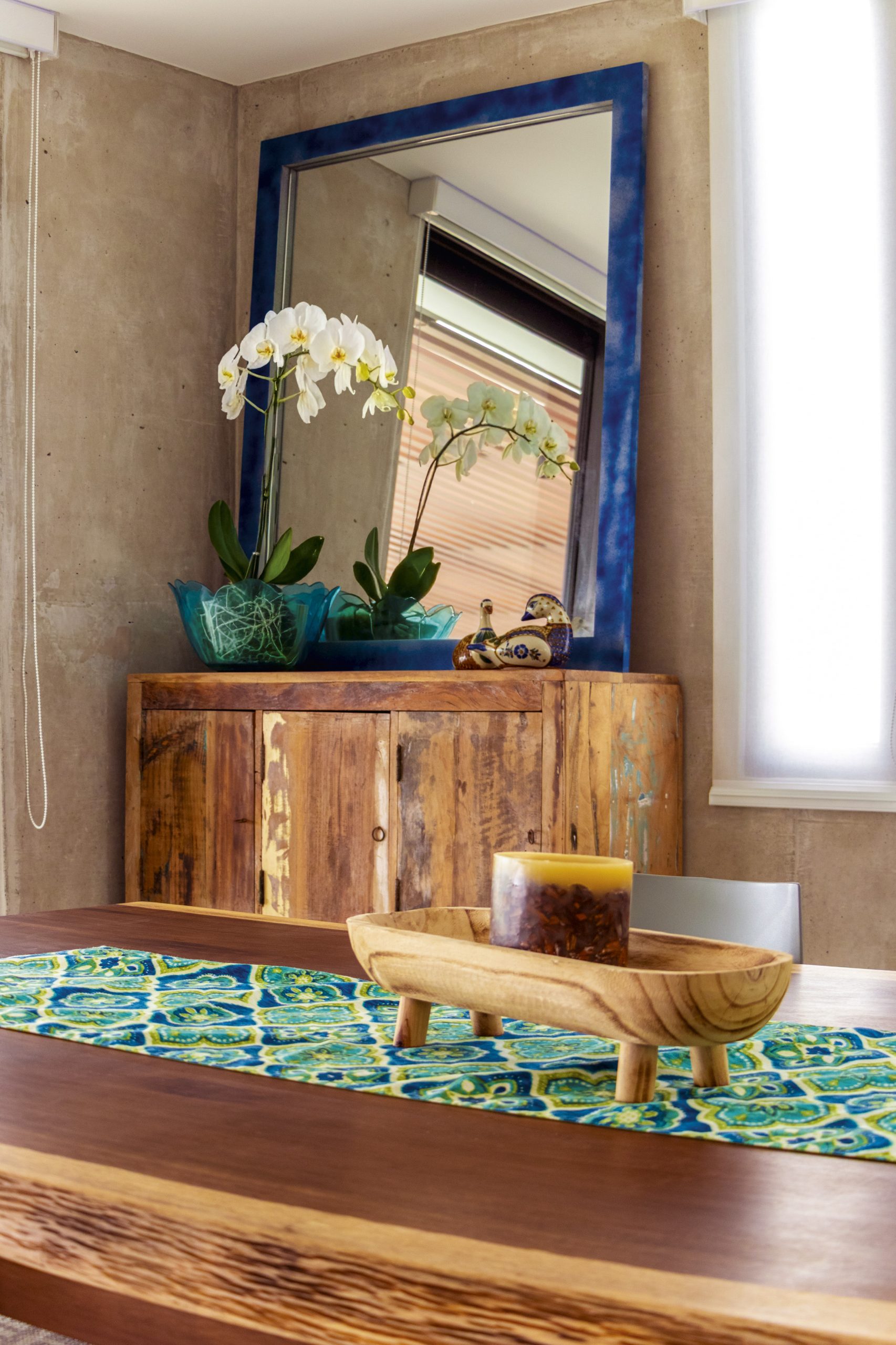 Un aparador de madera recuperada, orquídeas y piezas artesanales crean un punto focal que aporta color y carácter sin romper la armonía del espacio.