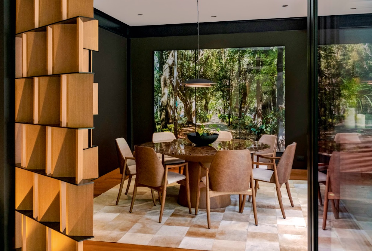 El comedor se despliega en dos escenas conectadas: adentro, la mesa Cona y las sillas Kevin, piezas de Sierra Muebles, dialogan con el arte y la estructura metálica.