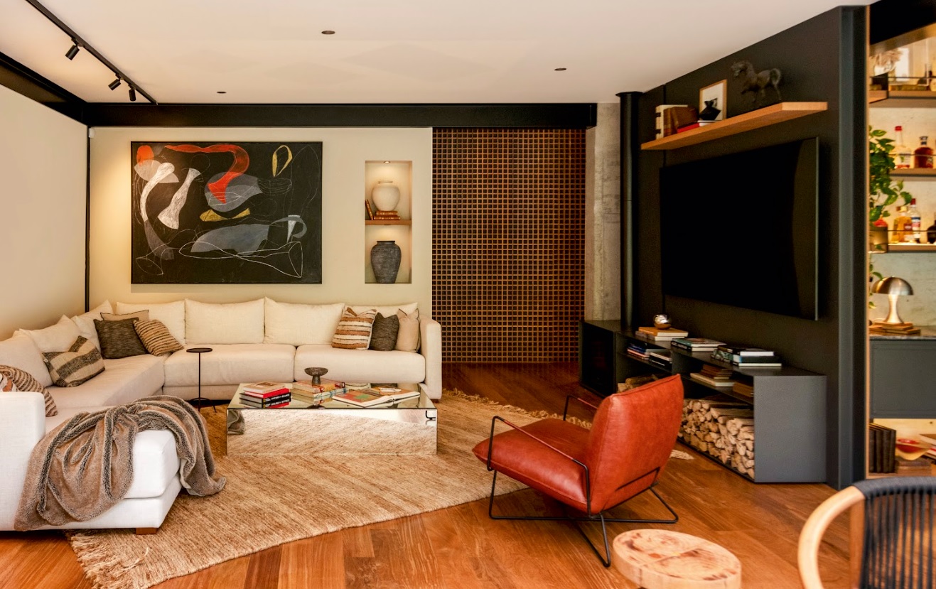 El núcleo de concreto articula chimenea y televisión en un solo frente limpio. Sofás amplios, madera y metal en equilibrio definen un ambiente contemporáneo y acogedor, pensado para reunirse y disfrutar.