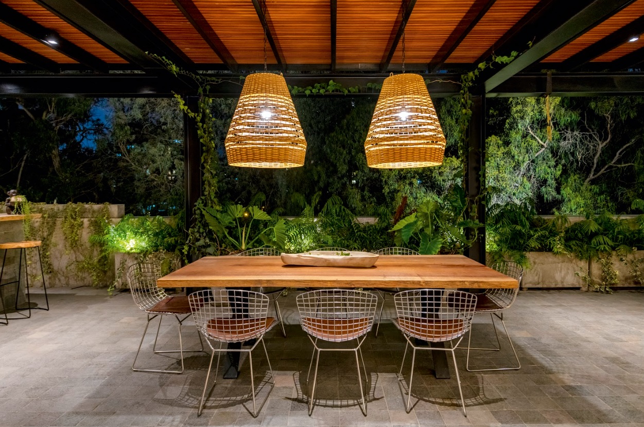 Las sillas Bertoya acompañan el comedor exterior que, bajo lámparas de fibras naturales, prolonga la experiencia social hacia el paisaje.